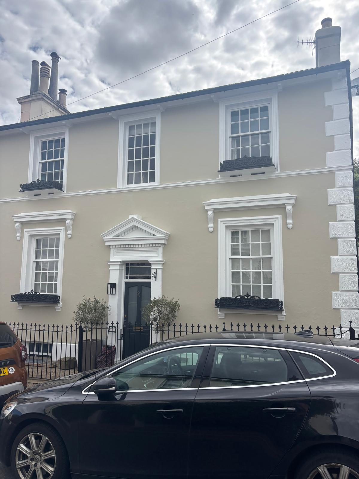 Period townhouse with white sash windows, black railings and a pale painted facade