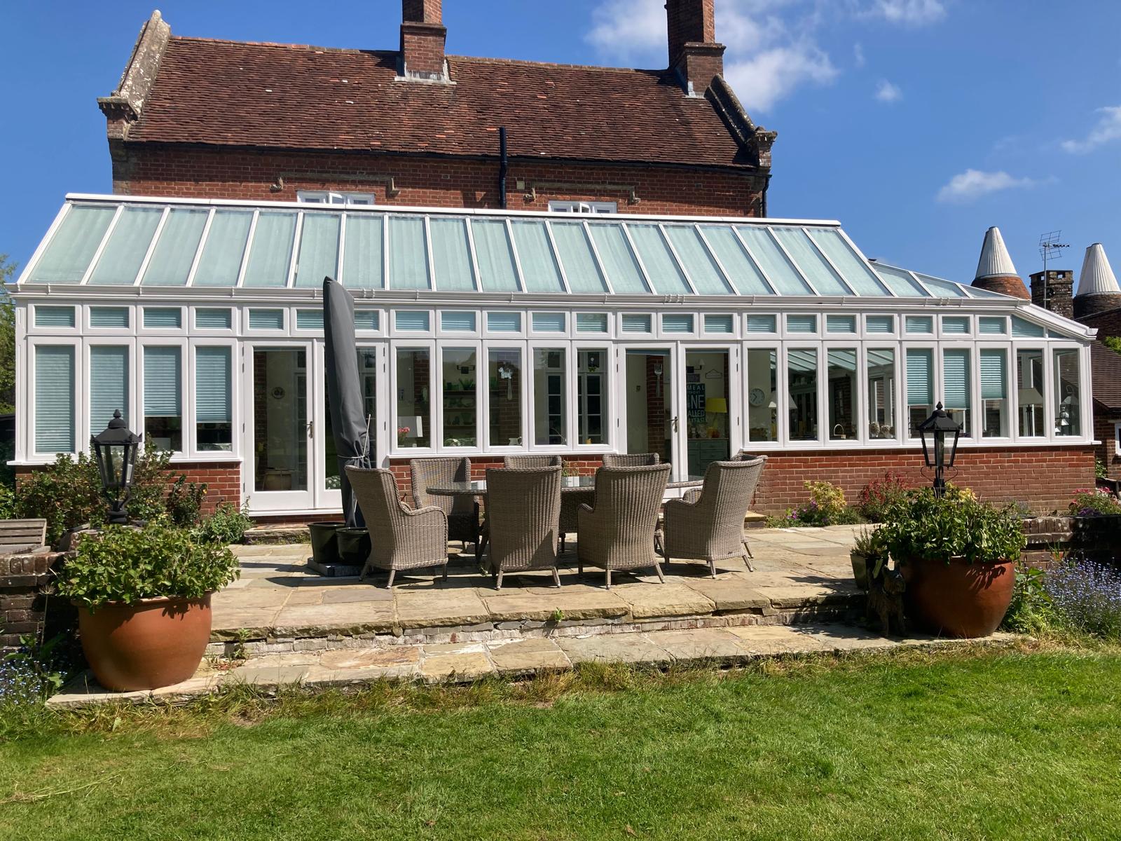 White-painted lean-to conservatory attached to a red-brick house, opening onto a stone patio